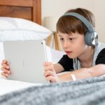 boy in blue shirt wearing headphones lying on bed